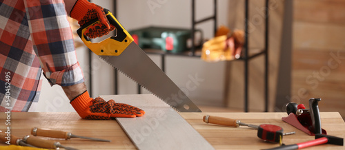 Photography Carpenter sawing wooden plank at table in workshop, closeup