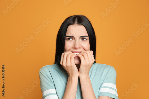 Young woman biting her nails on yellow background