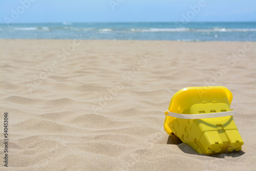 Yellow plastic bucket on sand near sea, space for text. Beach toy