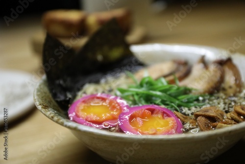 Bowl of ramen noodles with eggs, wakame salad and sesame seeds on table, closeup