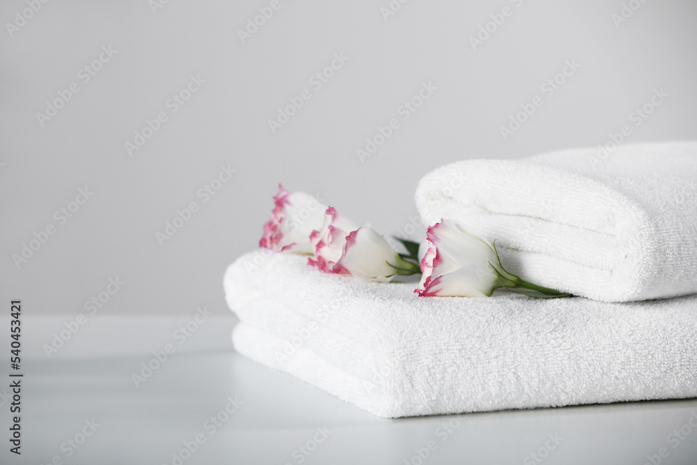 Folded soft towels with flowers on white table, space for text Folded soft towels with flowers on white table, space for text