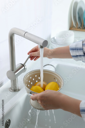 Woman washing fresh ripe lemons under tap water in kitchen, closeup