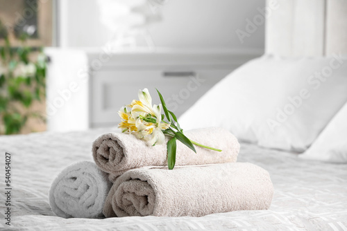 Fototapeta Naklejka Na Ścianę i Meble -  Terry towels with beautiful flowers on bed indoors, space for text