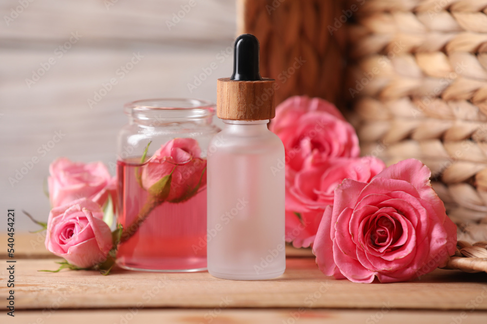 Bottles of essential rose oil and flowers on wooden table Bottles of essential rose oil and flowers on wooden table
