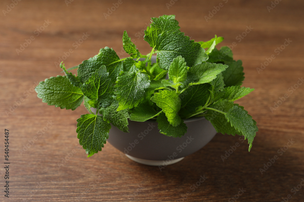 Fresh lemon balm in bowl on wooden table