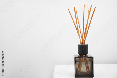 Aromatic reed freshener on table near white wall, space for text