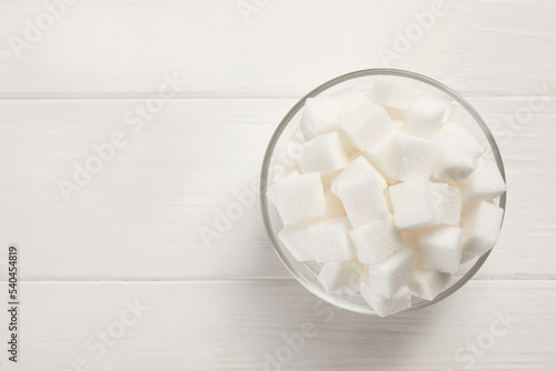 Bowl with sugar cubes on white table, top view. Space for text