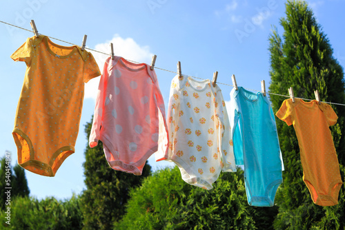 Clean baby onesies hanging on washing line in garden. Drying clothes