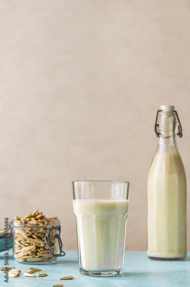 Sunflower milk in a glass and bottle, raw sunflower seeds in jar on light blue background