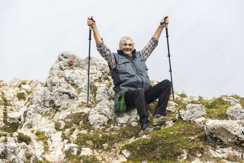 Senior Man With Raised Hands Sitting Tired but Happy on the Top of Alpine Trial to Slemenova Spica in Julian Alps