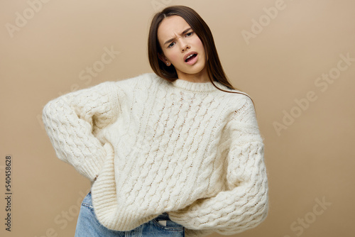 an outraged woman stands and looks straight at a light brown background in a white sweater, looking disgustedly with two hands on her belt photo