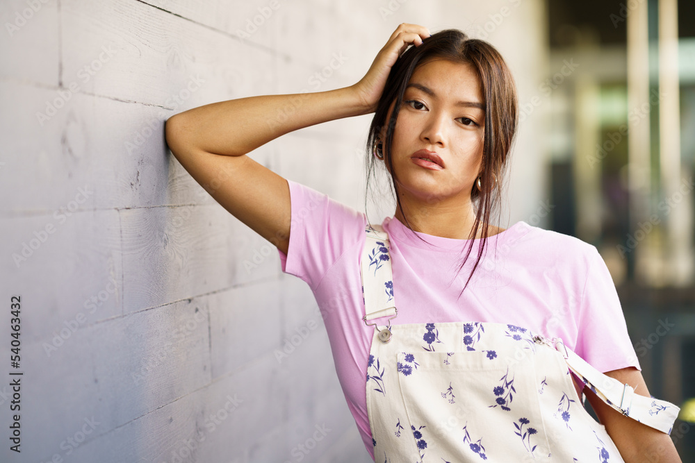Attractive Chinese girl looking at camera with serious expression leaning against an urban wall Attractive Chinese girl looking at camera with serious expression leaning against an urban wall