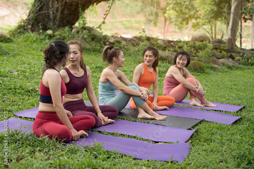 A group of young women are practicing yoga beside the mountain by the stream in the morning.