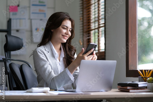 Young smiling business woman using smartphone near computer in office  copy space