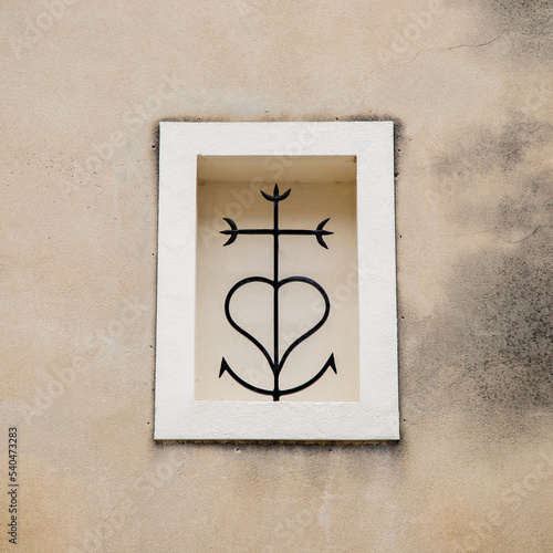 Croix de Camargue sur façade de maison de village.