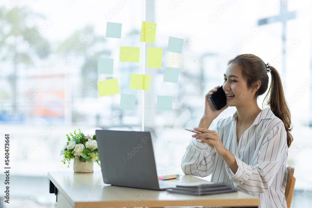 Attractive Asian businesswoman in office working on laptop and using smartphone to stay in touch with colleagues or clients. Attractive Asian businesswoman in office working on laptop and using smartphone to stay in touch with colleagues or clients.