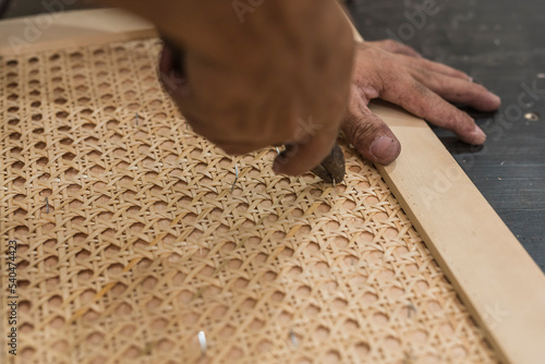 A carpenter removes staples from a rattan solihiya design with a pair of pliers. A rattan furniture workshop. photo