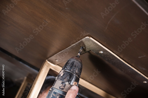 A man uses a screw gun to drive screws into the underframe of a table. Furniture making concept. photo