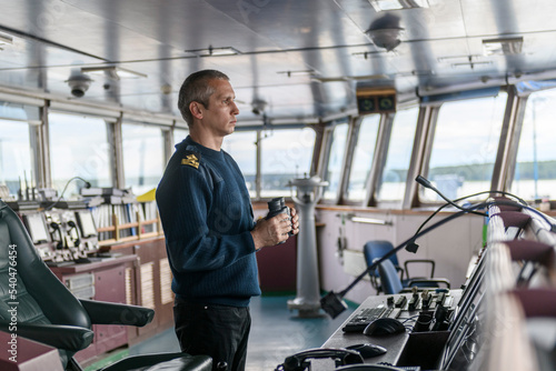 Deck officer with binoculars on navigational bridge. Seaman on board of vessel. Commercial shipping. Cargo ship.