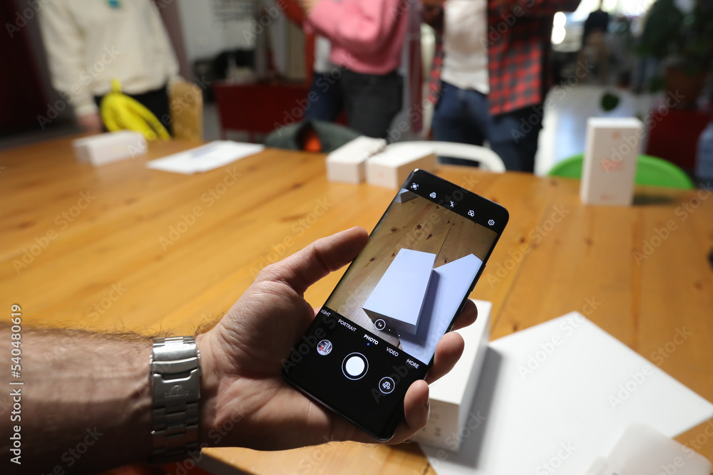 © Silviu - A man films with his mobile phone a white box sitting on a table. Person photographs using in hands mobile phone, closeup.