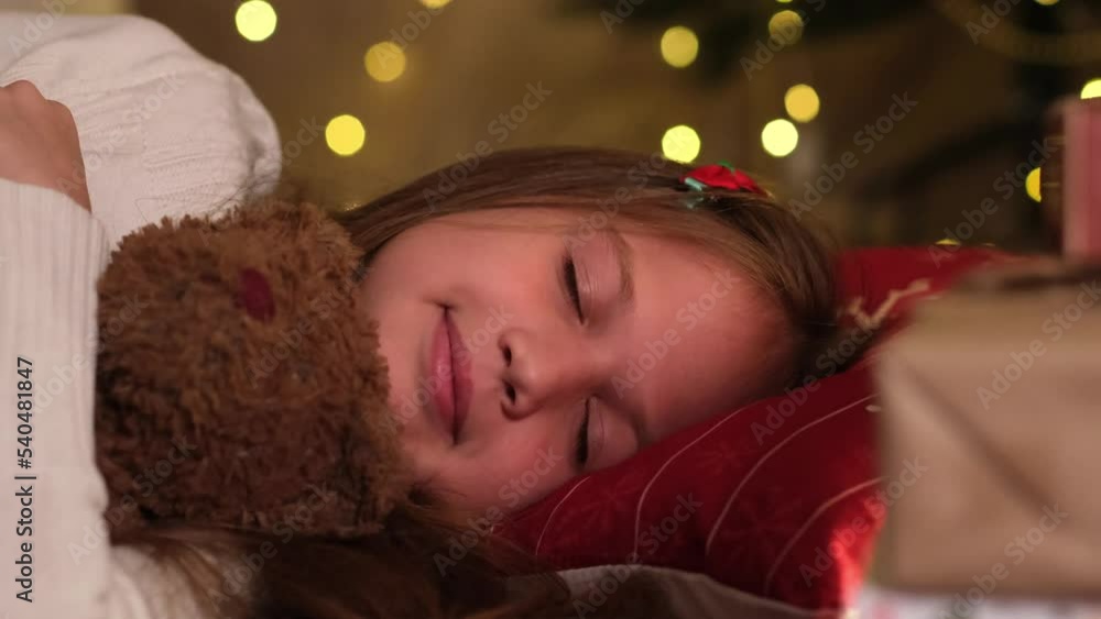 Happy smiling little girl at Christmas or New Year's Eve sleeping waiting for gift for holiday from Santa Claus. Traditional family celebration, childhood and children dreams. Close up Happy smiling little girl at Christmas or New Year's Eve sleeping waiting for gift for holiday from Santa Claus. Traditional family celebration, childhood and children dreams. Close up