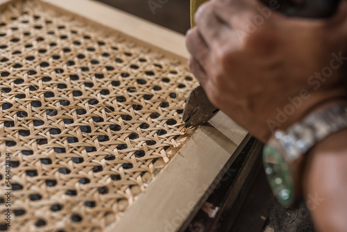 A carpenter removes staples securing a rattan solihiya screen from a wooden frame with a pair of pliers. A rattan furniture workshop. photo