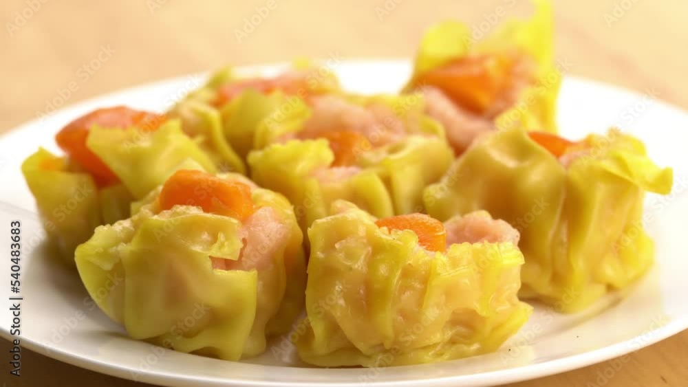 Closeup view rotation of fresh delicious homemade shrimp, minced pork and salted egg yolk steamed dumplings in white ceramic dish on wooden board. Closeup view rotation of fresh delicious homemade shrimp, minced pork and salted egg yolk steamed dumplings in white ceramic dish on wooden board.