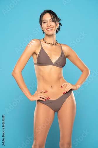 Happy Woman In Bikini With Suntan Lotion Shaped Sun On Her Shoulder, On A Blue Background.
