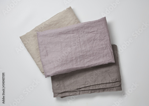 Stack of linen fabric texture of tablecloths on a white background. Natural linen organic canvas background. Dark grey, lilac, beige linen kitchen textile. 