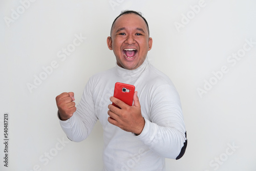 Asian muscular man looking camera with excited expression when holding handphone photo