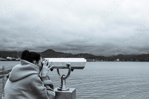 a girl watching through stationary binoculars on the pier for passing ships and wildlife on the seashore