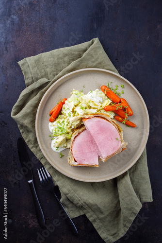 Gebackenes Kasseler Schweinesteak im Teigmantel mit Wirsing Kohl und Baby Karotten serviert als Draufsicht auf einem Design Teller mit Textfreiraum photo