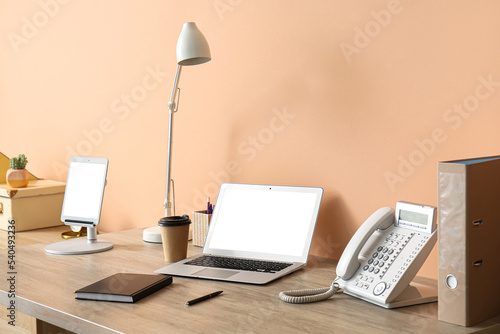 Laptop, paper cup of coffee, lamp, tablet computer, notebook and landline phone on standing desk