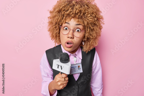 Φωτογραφία Amazed curly haired European woman stares impressed at camera works as professional reporter records live stream tells news dressed in formal clothes isolated over pink background