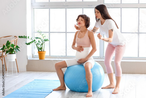 Young woman and her pregnant wife training with fitball at home