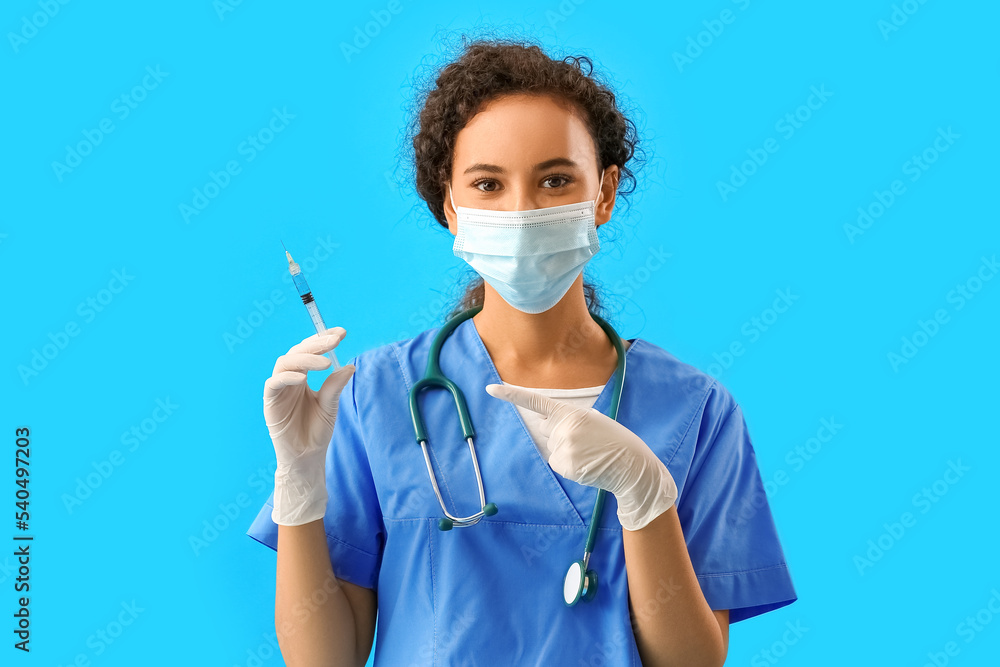 Female doctor in medical mask pointing at syringe on blue background