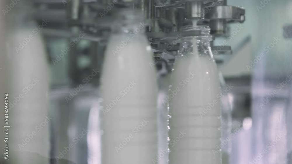 Automated production line at the Dairy Food Facility. Multiple plastic milk bottles are being filled with milk on an automated production line. Pouring milk on automated production line. Automated production line at the Dairy Food Facility. Multiple plastic milk bottles are being filled with milk on an automated production line. Pouring milk on automated production line.