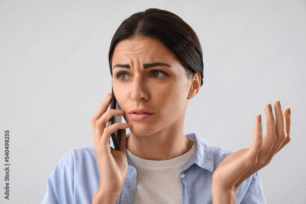Stressed young woman talking by mobile phone on light background Stressed young woman talking by mobile phone on light background