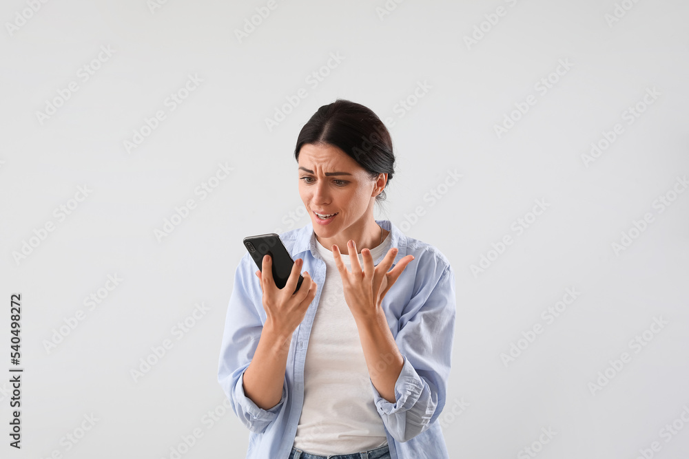 Stressed young woman with mobile phone on light background Stressed young woman with mobile phone on light background