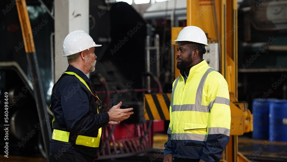 Engineers in discussion in machine maintenance in factory. Group of Industrial Engineers with Blueprint against trains and machinaries industry background. Studying Blueprint with Superior Engineers in discussion in machine maintenance in factory. Group of Industrial Engineers with Blueprint against trains and machinaries industry background. Studying Blueprint with Superior