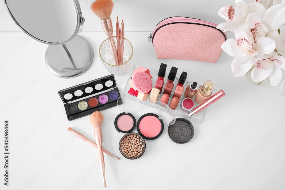 Organizer with cosmetics, bag, mirror and flowers in vase on table near light wall Organizer with cosmetics, bag, mirror and flowers in vase on table near light wall