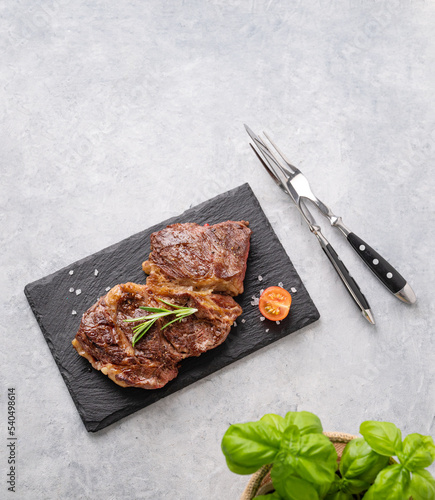 BBQ grilled beef steak with pepper, rosemary and basil on black slate on light background.