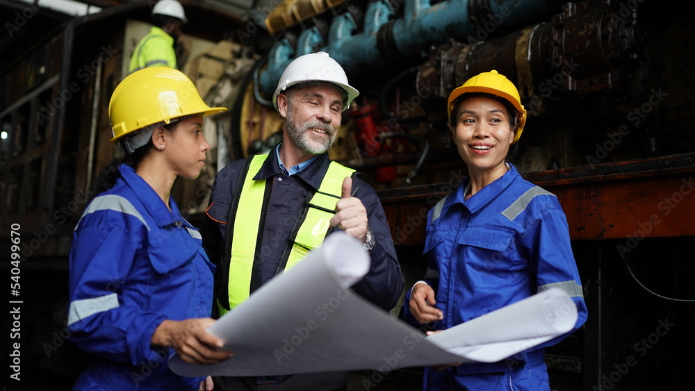 Fototapeta premium Engineers in discussion in machine maintenance in factory. Group of Industrial Engineers with Blueprint against trains and machinaries industry background.