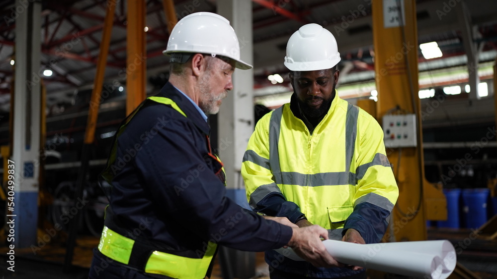 Engineers in discussion in machine maintenance in factory. Group of Industrial Engineers with Blueprint against trains and machinaries industry background. Studying Blueprint with Superior Engineers in discussion in machine maintenance in factory. Group of Industrial Engineers with Blueprint against trains and machinaries industry background. Studying Blueprint with Superior