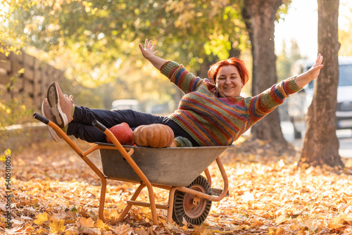 Fotobehang Woman have fun, lying in the garden wheelbarrow with pumpkins