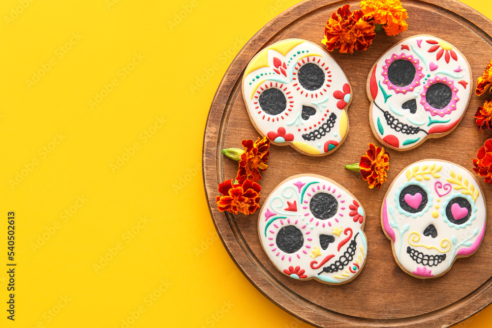 Fototapeta premium Board with skull shaped cookies and flowers on yellow background. El Dia de Muertos