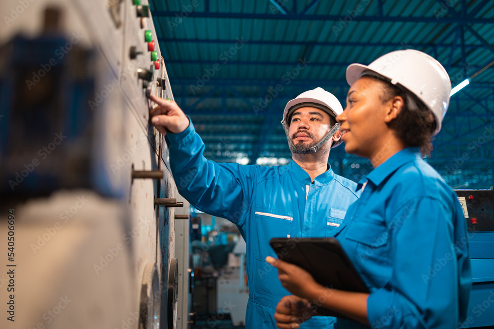 Engineer senior asian man and african woman wearing safety helmet working and checking machine automotive part warehouse. Factory for the manufacture and electric processing. Engineer senior asian man and african woman wearing safety helmet working and checking machine automotive part warehouse. Factory for the manufacture and electric processing.