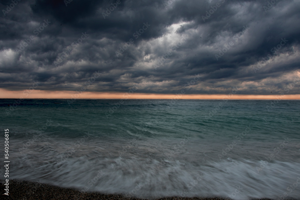 Black clouds and a turbulent sea are reflected off the beach as the sunlight draws a pink line on the horizon. Varigotti, Liguria, Italy. Long exposition.