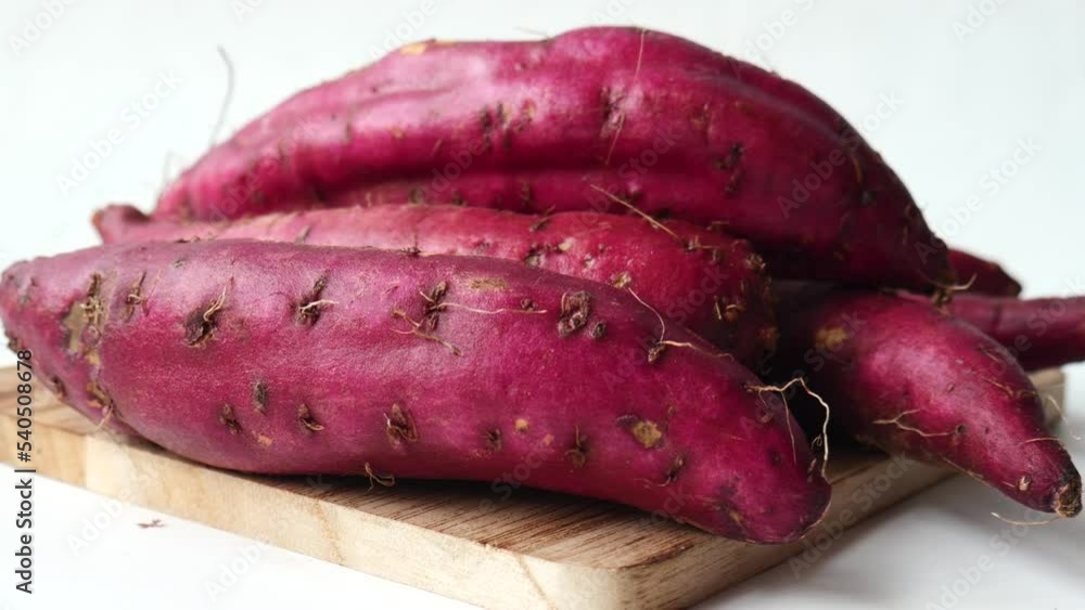 Close up of raw sweet potato on chopping board on white background Close up of raw sweet potato on chopping board on white background