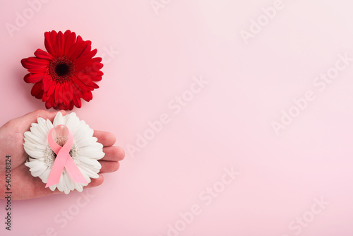 Pink Breast Cancer Awareness Ribbon. Hands holding red gerbera and pink ribbon on backgrounds. Breast cancer awareness and October Pink day  world cancer day. Top view. Mock up.